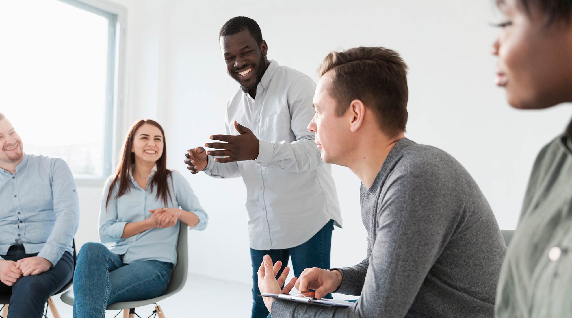 Success & Wellbeing Service Page Group Therapy Offers Telehealth in New York, Massachusetts & Maine image of smiling man talking to a group