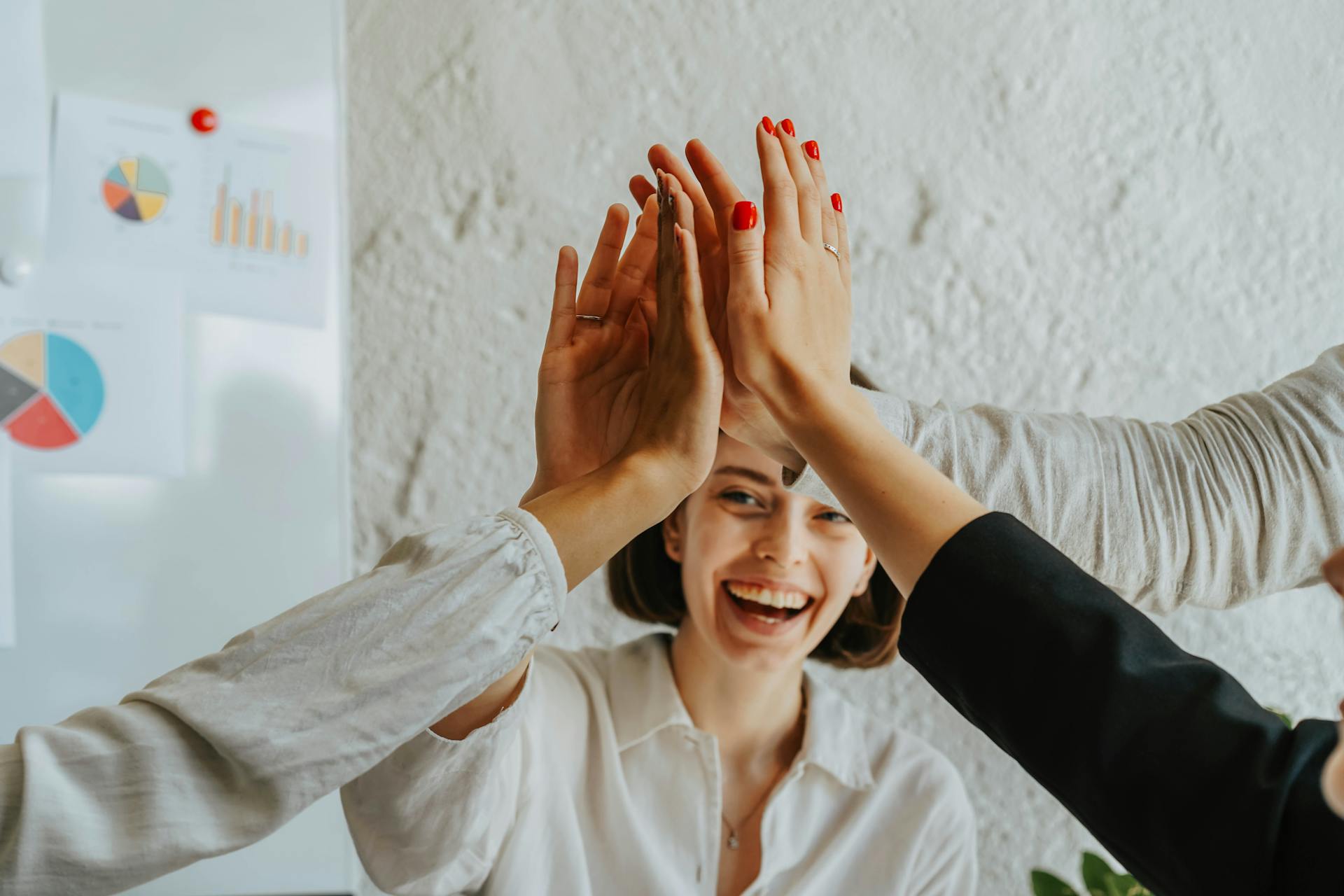 People giving a group high-five with a smiling woman in the background, representing teamwork, encouragement, and motivation in group therapy sessions.