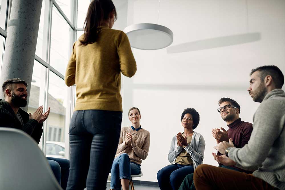 A person stands in a circle of people who are sitting and clapping.