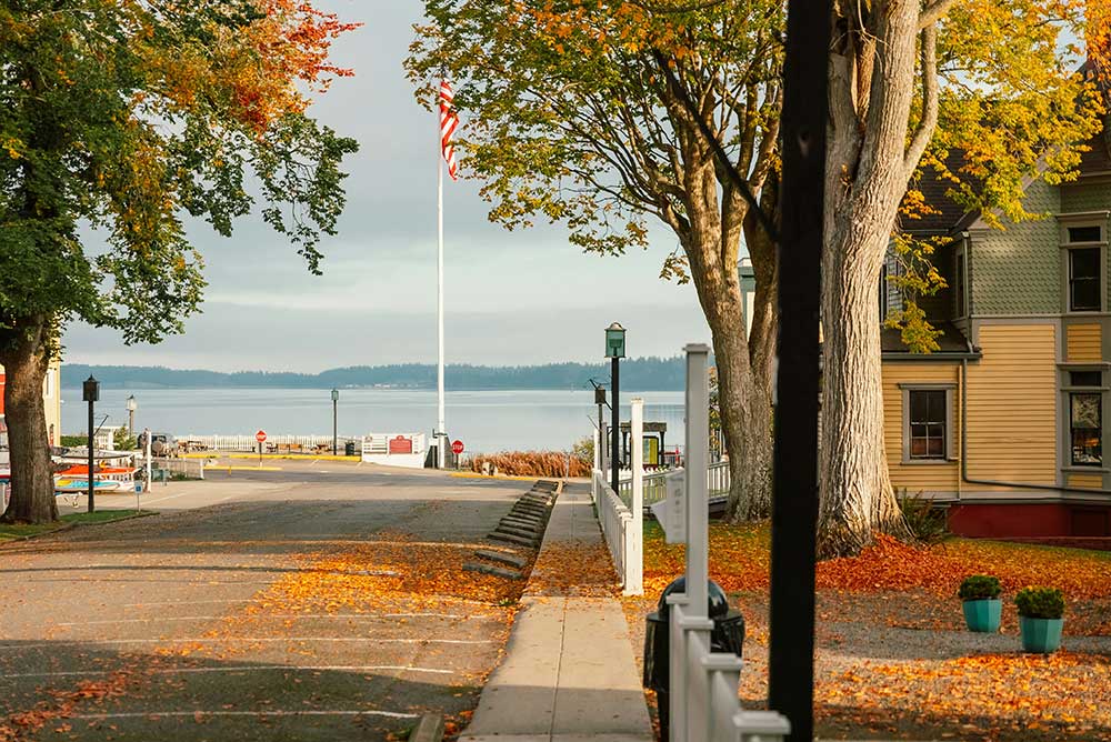 A town street in autumn leads to a waterfront.