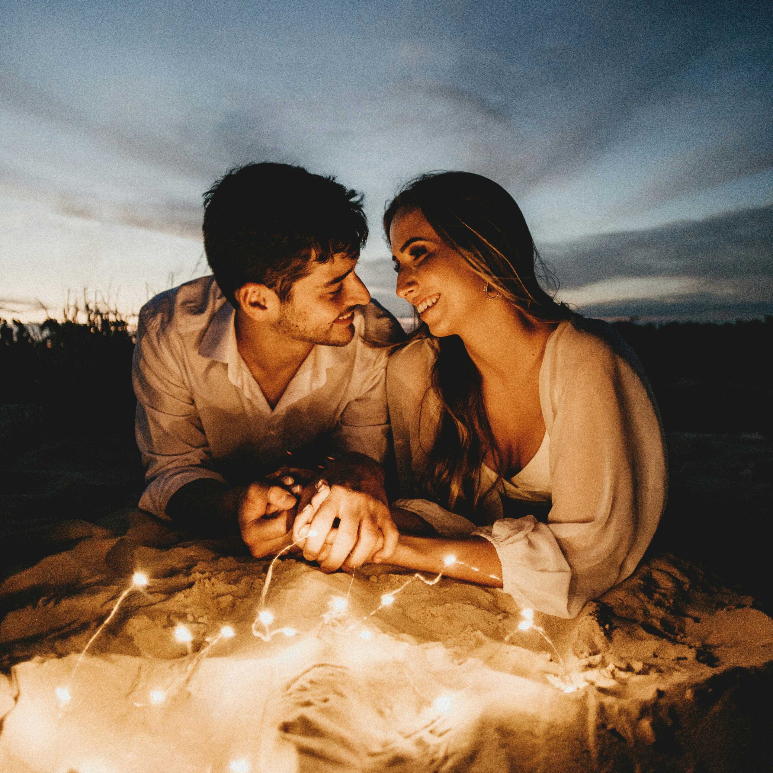 Couple lying down holding hands with fairy lights under a night sky