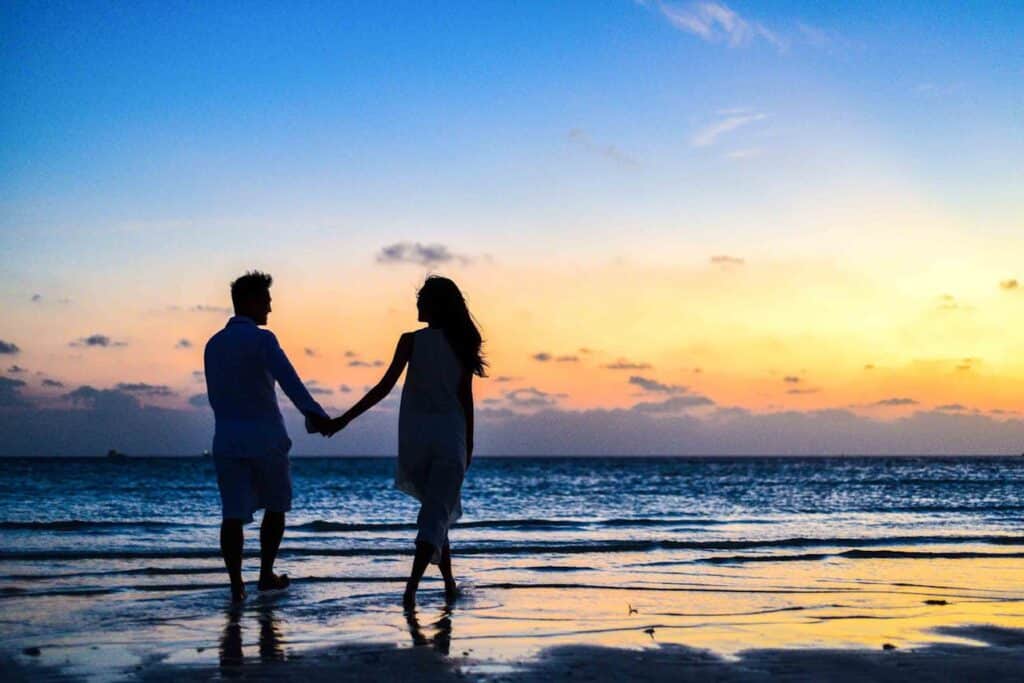 Couple holding hands while walking on the beach during sunset