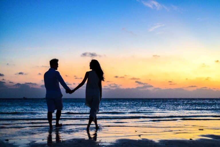 Couple holding hands while walking on the beach during sunset