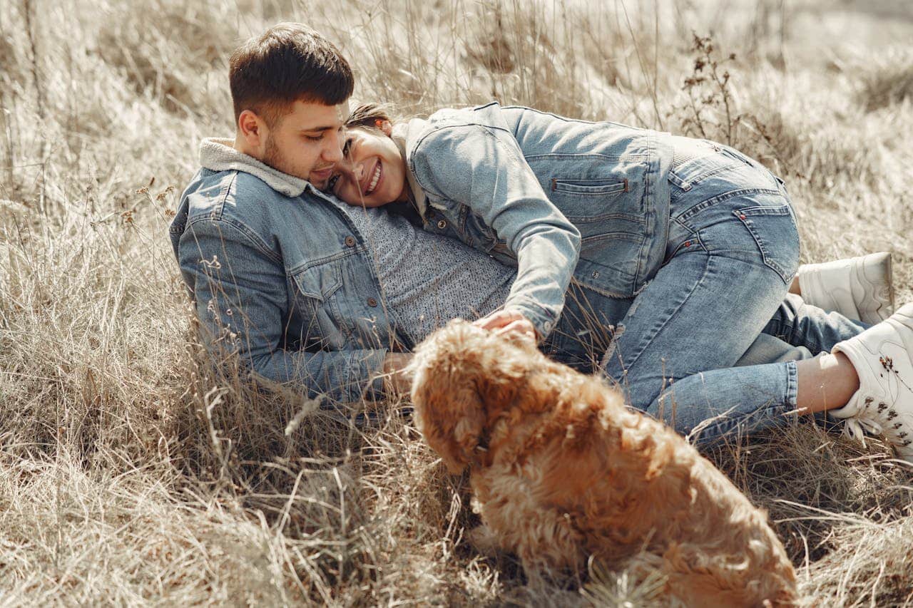 A couple relaxing together in a field with their dog, showing closeness and emotional connection.