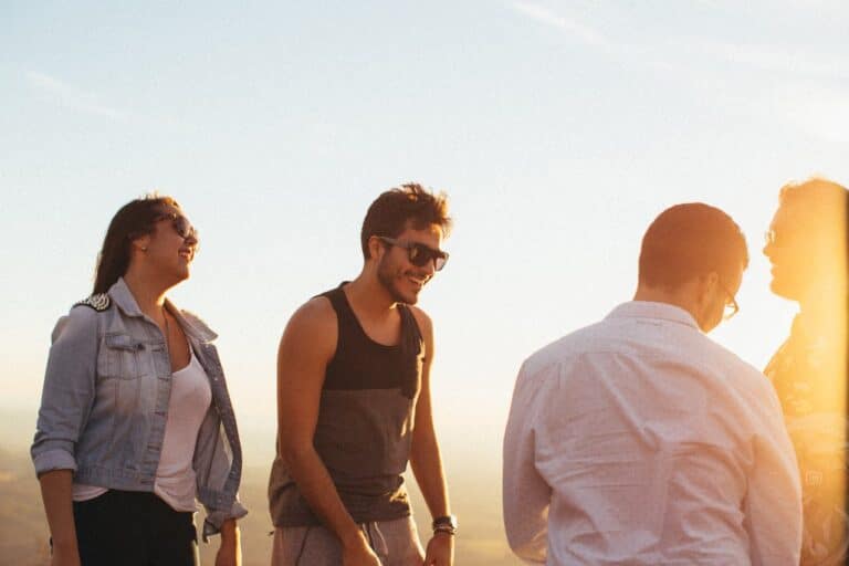 A small group of adults standing together outdoors, smiling and talking during sunset, representing connection and support in group therapy.