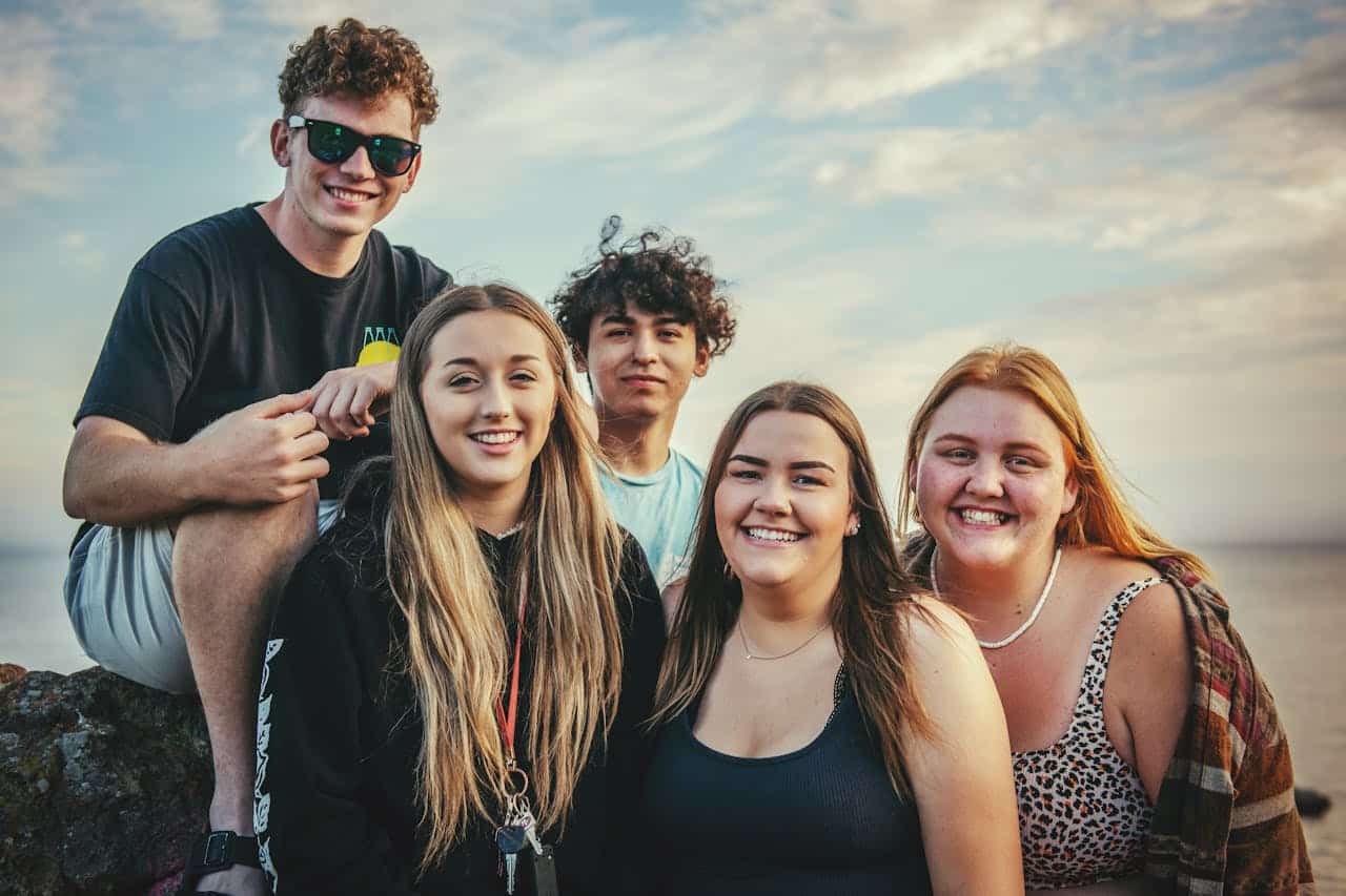 A group of young adults smiling and sitting together outside, symbolizing community, belonging, and shared growth in group therapy.