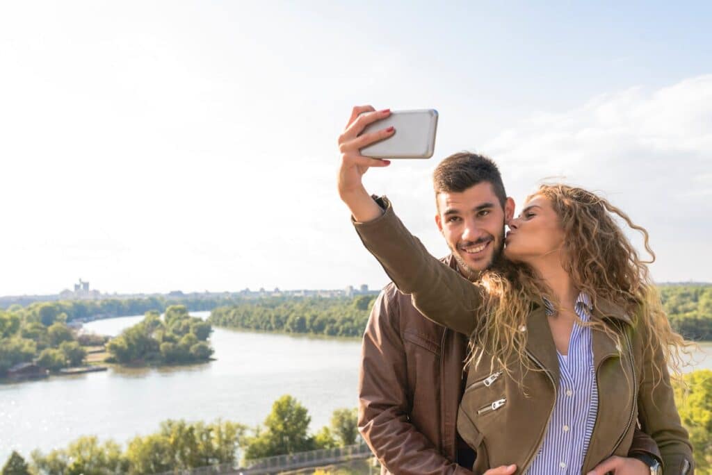 Couple taking a selfie outdoors while sharing a kiss, symbolizing connection and relationship growth.