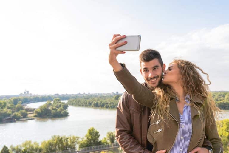 Couple taking a selfie outdoors while sharing a kiss, symbolizing connection and relationship growth.