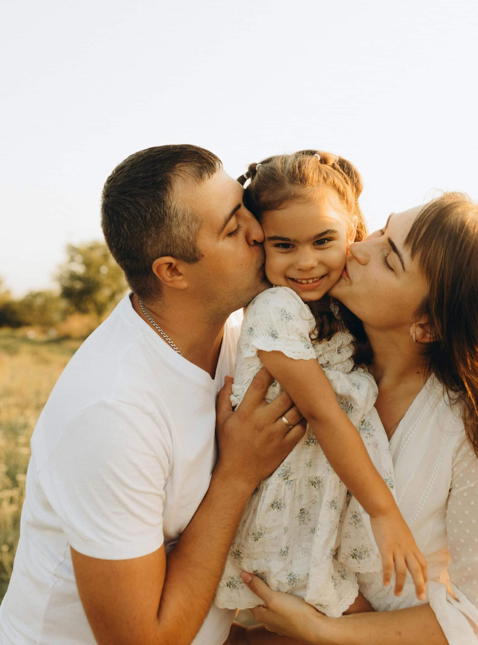 Mother and father kissing their daughter on both cheeks, a joyful family moment filled with affection and closeness