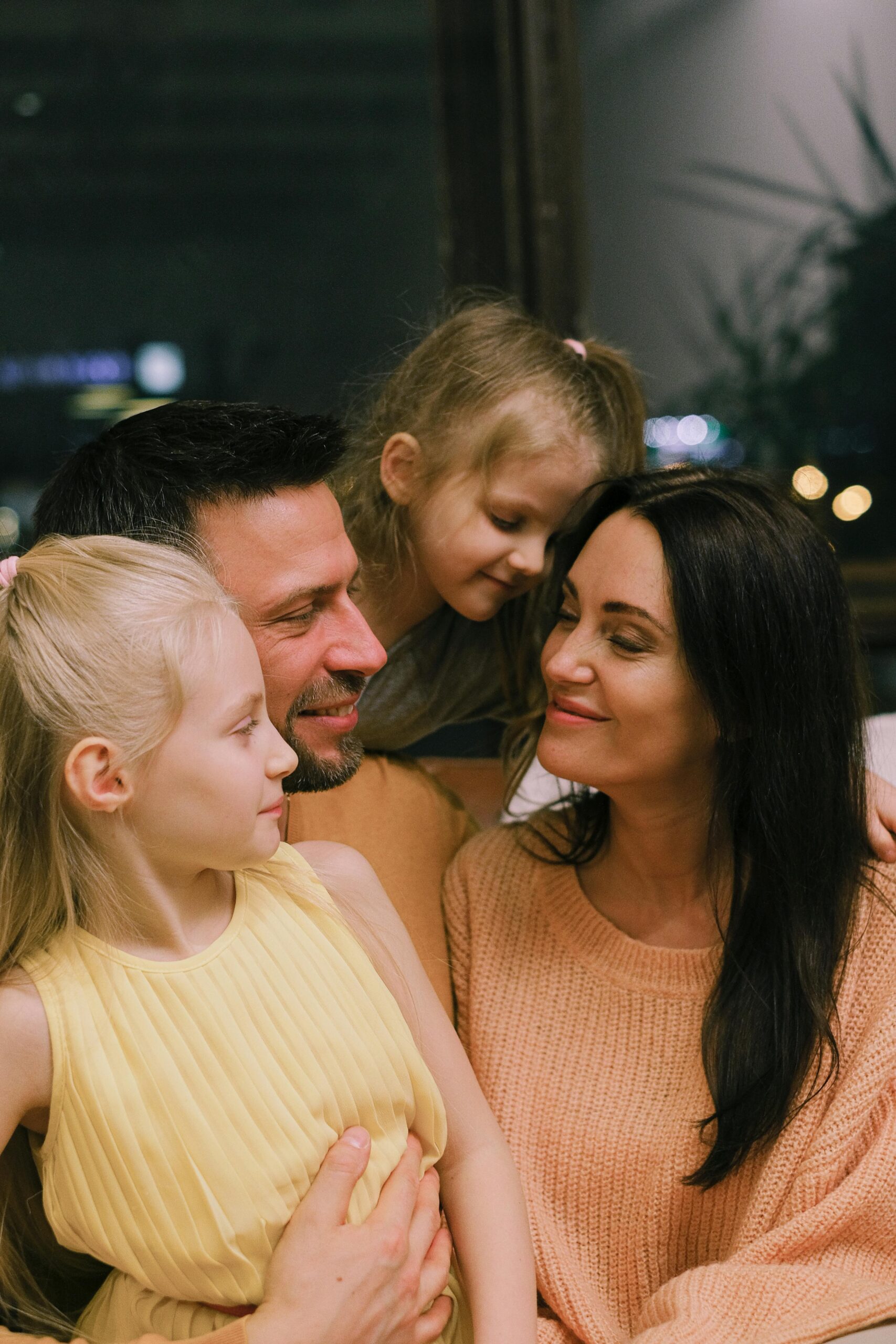 Parents standing close with their two daughters, relaxed posture and smiles reflecting family harmony