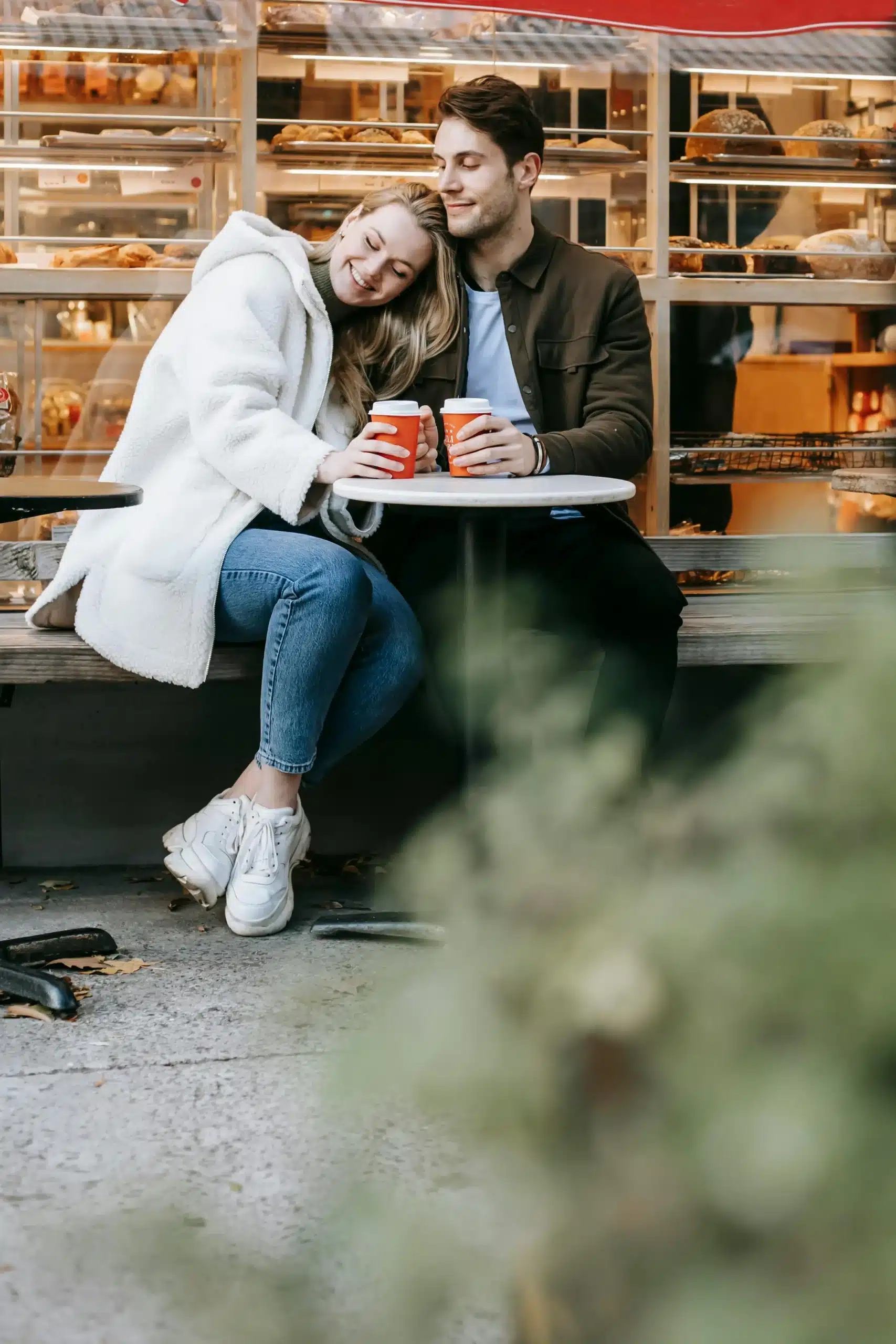  A couple sitting together at a café table with coffee, smiling warmly and enjoying a relaxed conversation in daylight