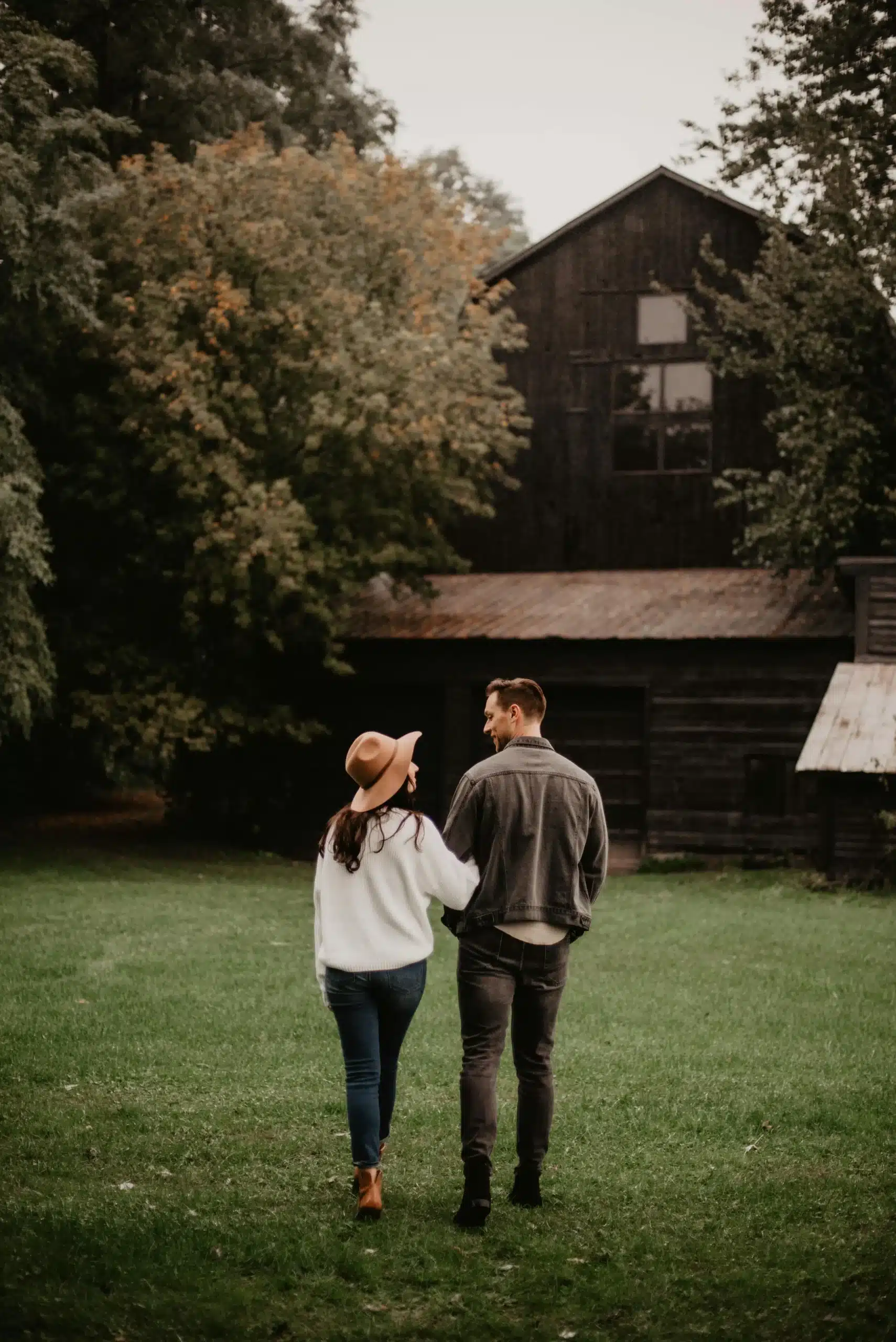 A couple standing outside a cozy cottage surrounded by trees, looking at each other with warmth and affection