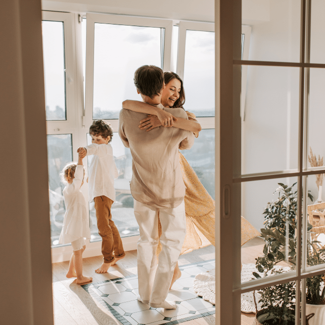 Parents hugging while children dance nearby, expressing love, connection, and a joyful, emotionally safe environment.