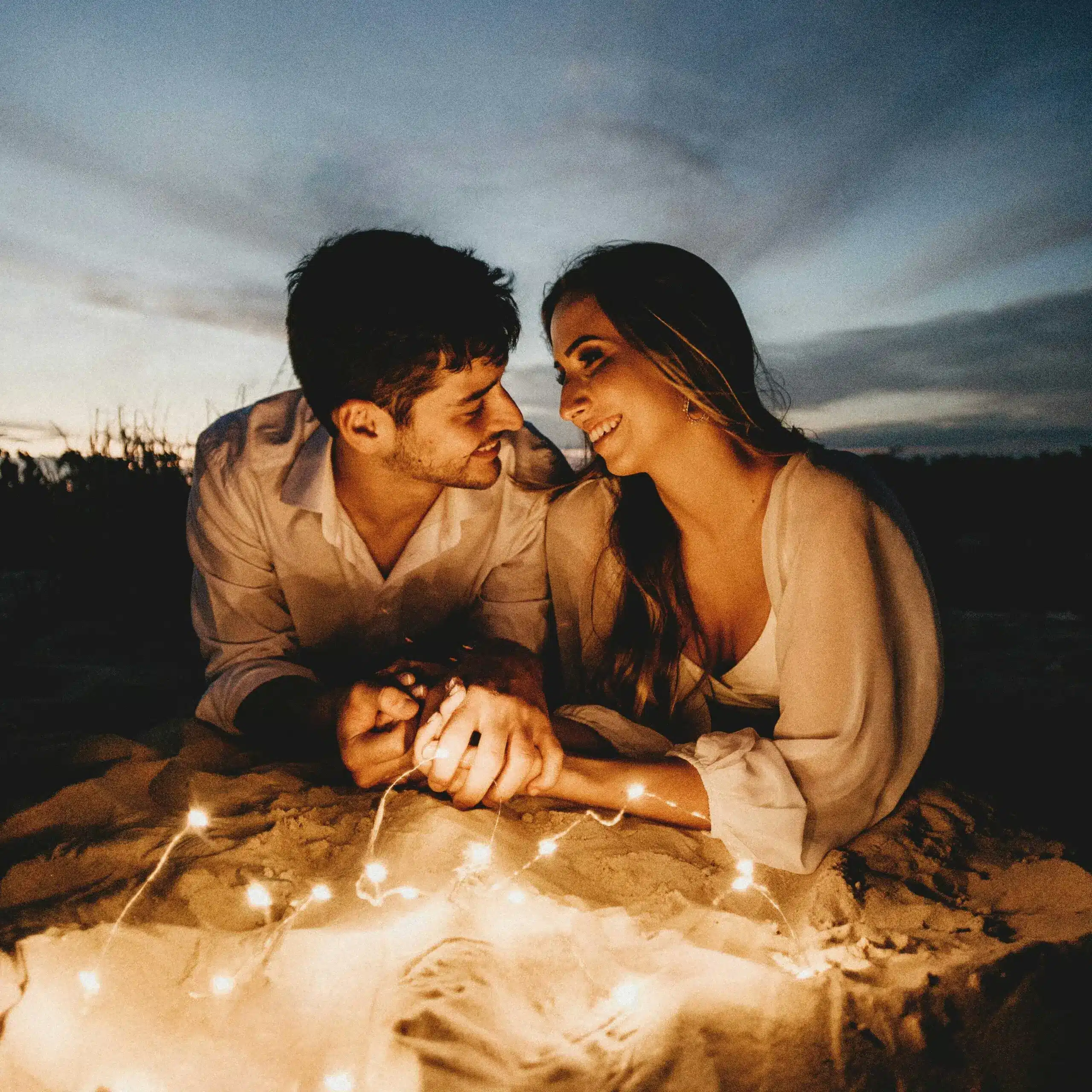 Couple lying down holding hands with fairy lights under a night sky