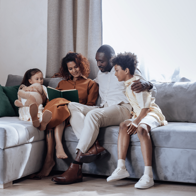 A family sitting together reading a book symbolizes shared learning, bonding, and nurturing connection at home.