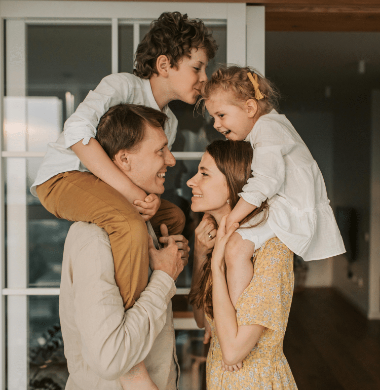 Parents standing with children on their shoulders, smiling, expressing joy, connection, and strong family bonds.
