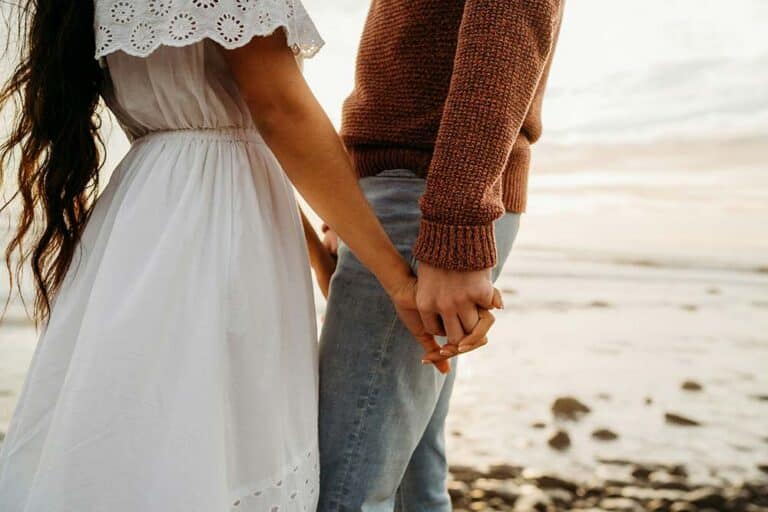 Couple holding hands together while walking on the beach.